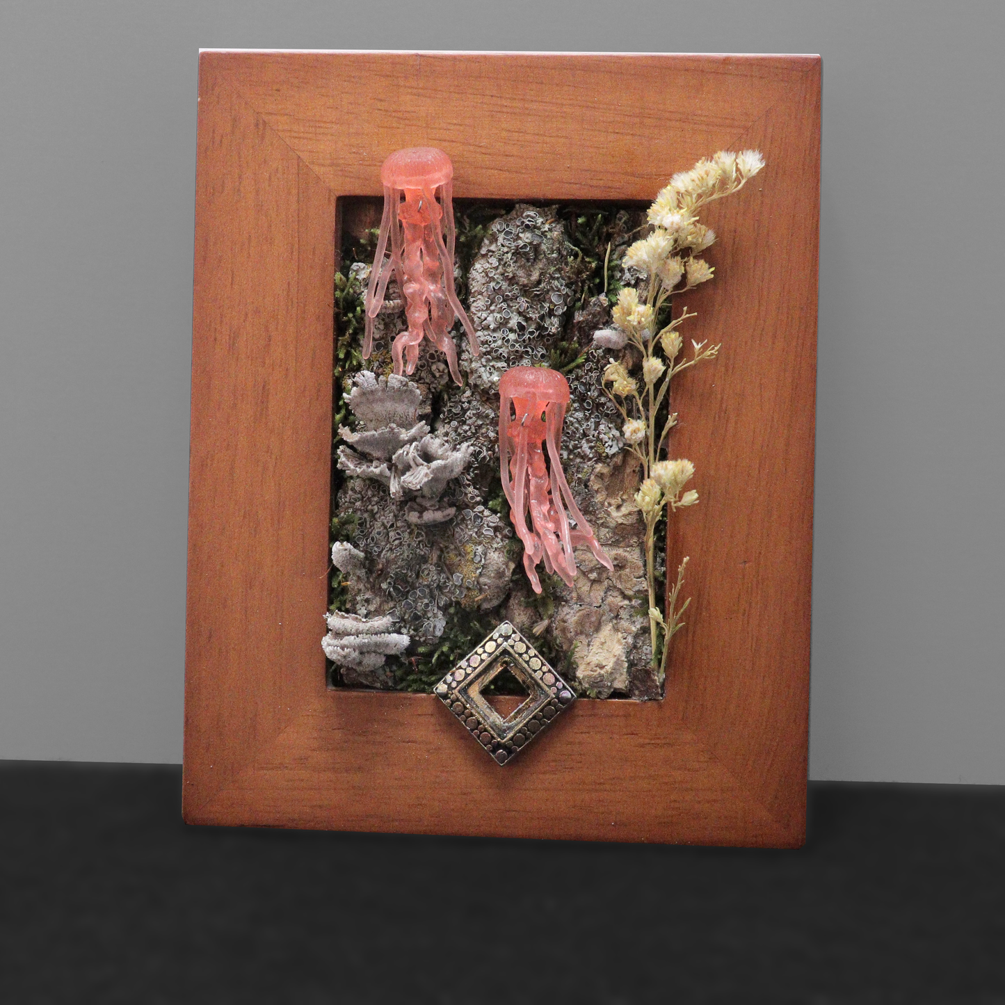 Decorative wall art with pink jellyfish, dried plants, and a decorative stone in a wooden frame.