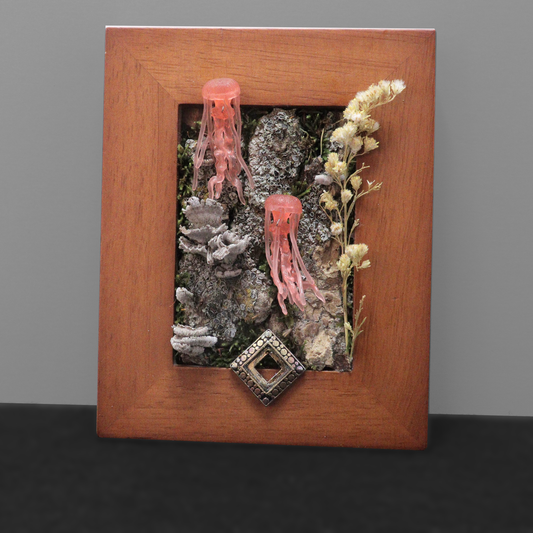 Decorative wall art with pink jellyfish, dried plants, and a decorative stone in a wooden frame.