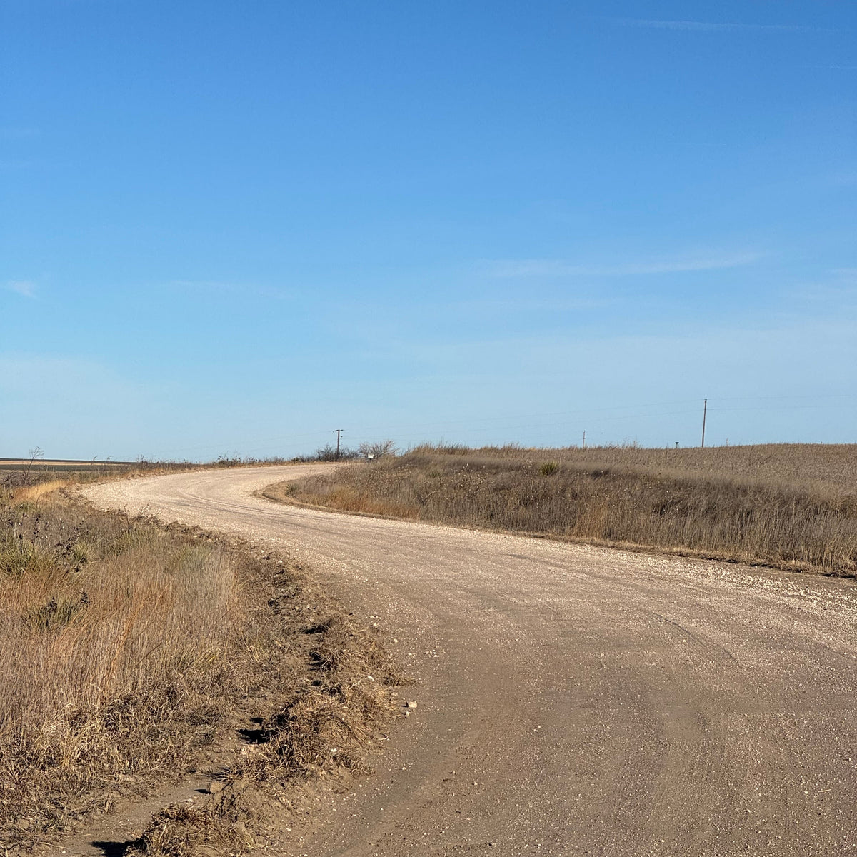 Narrow dirt road curving through a dry landscape with a clear blue sky.
