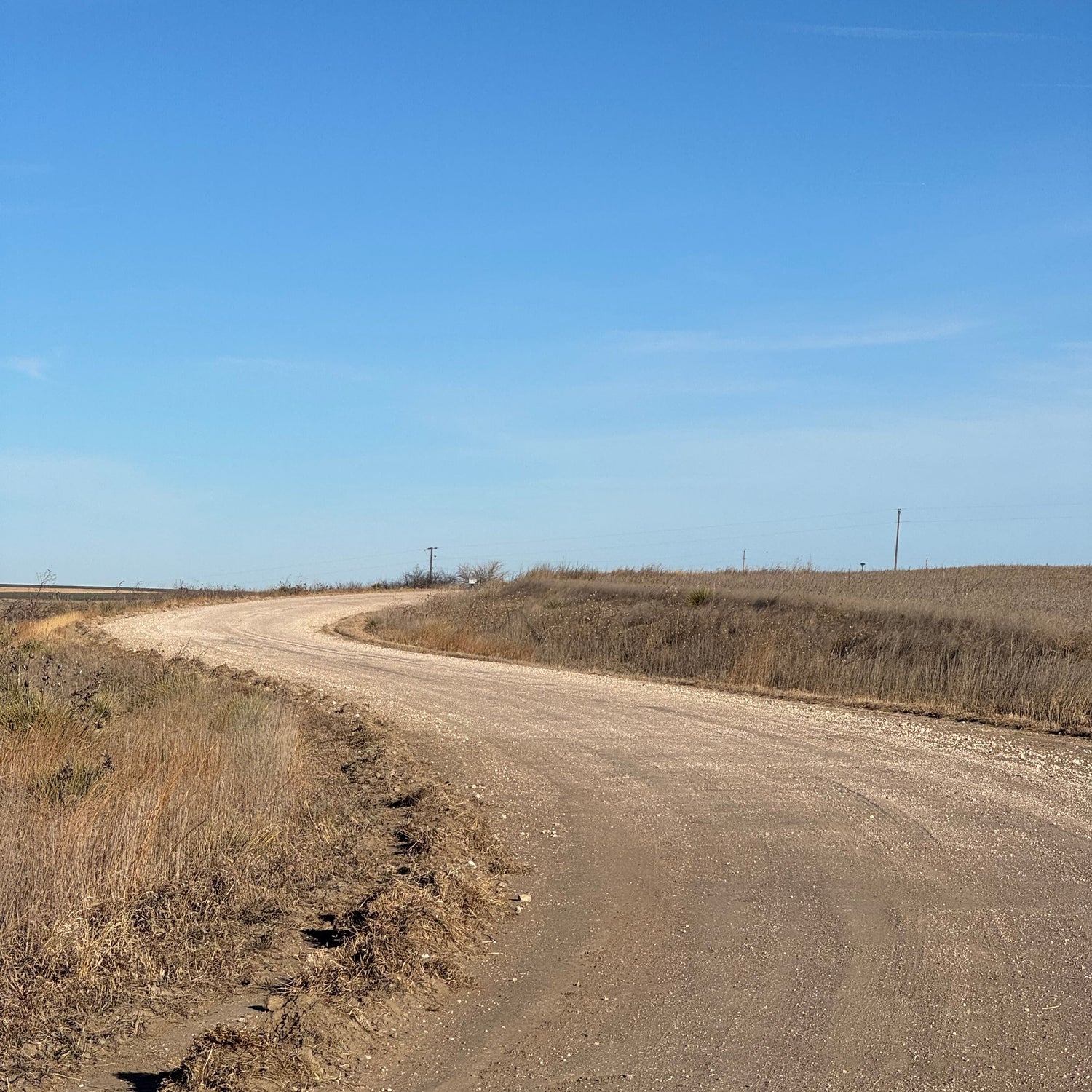 Narrow dirt road curving through a dry landscape with a clear blue sky.