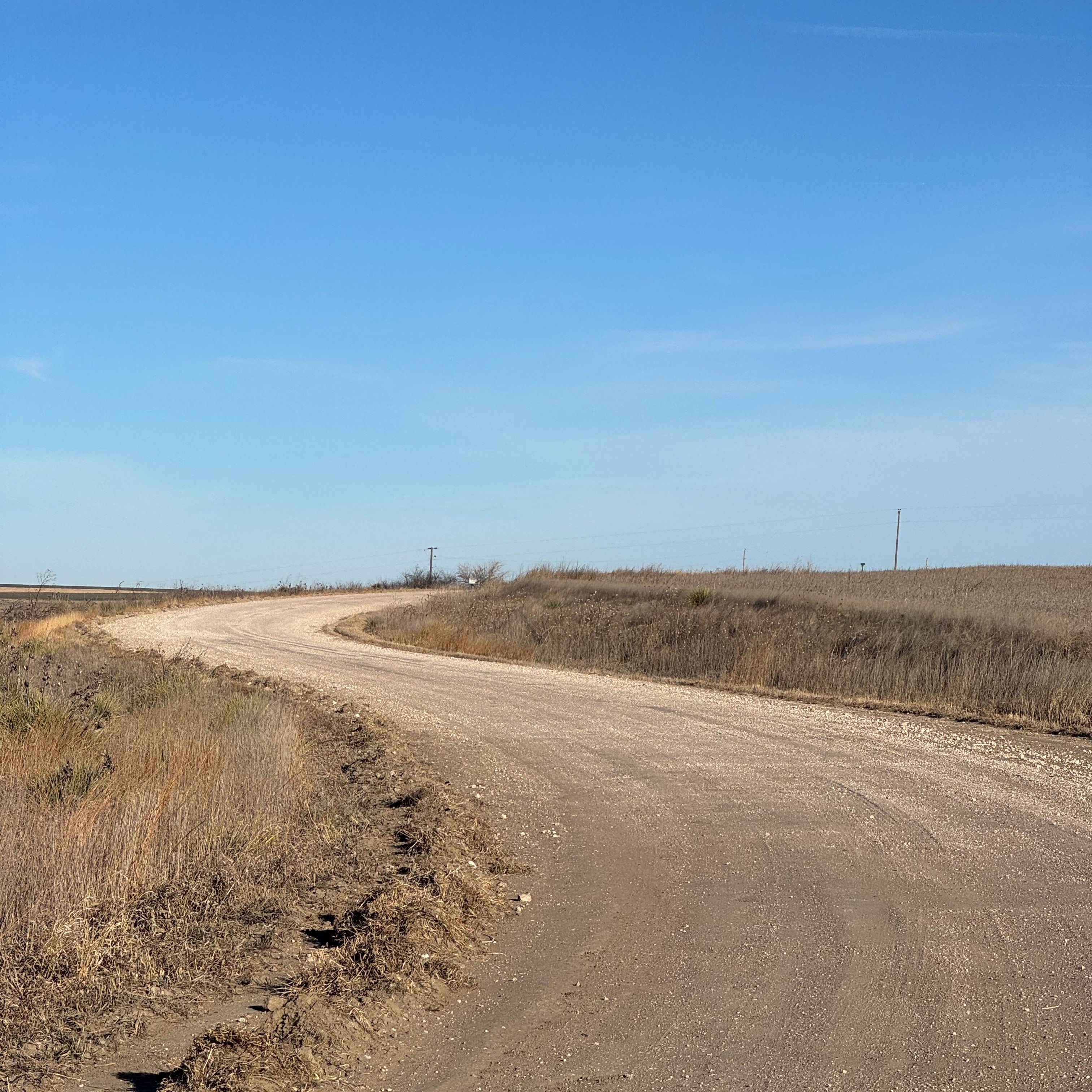 Narrow dirt road curving through a dry landscape with a clear blue sky.