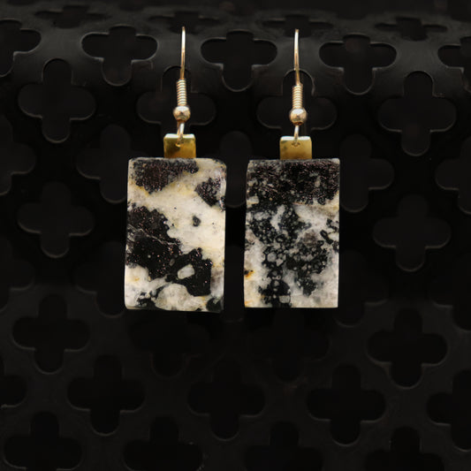 Square stone earrings with gold accents on a black textured background