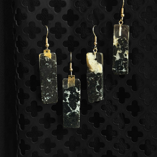 Set of four earrings with rectangular black and white stone-like pendants on a black textured background.