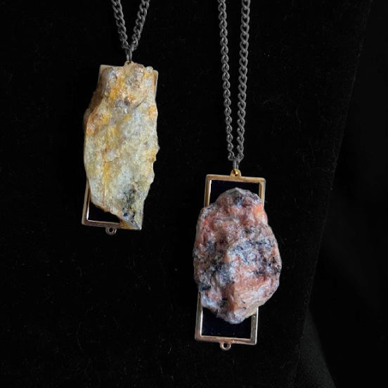 Two stone pendants on chains against a black background