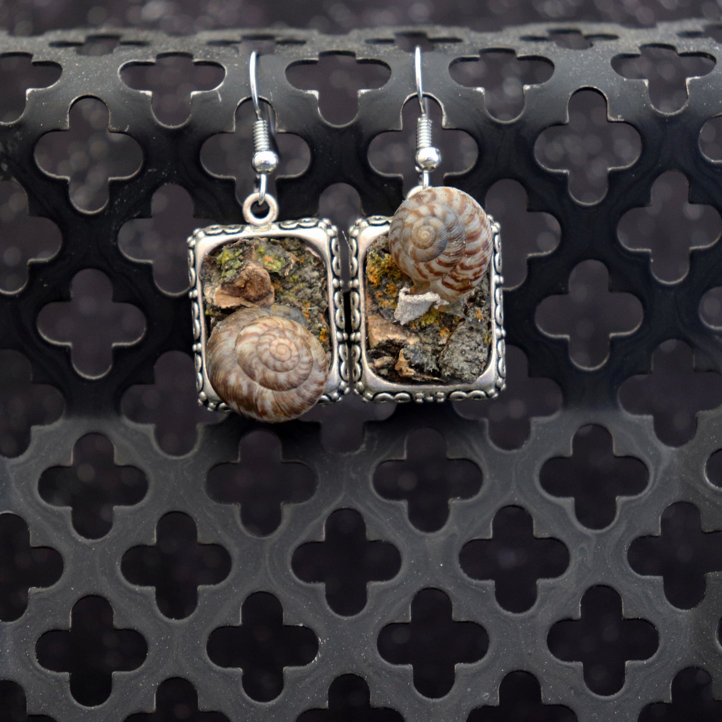 Pair of square earrings with natural stone and shell designs on a textured black background